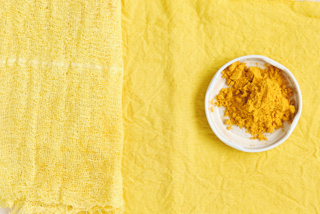 Yellow powder in a white bowl on a yellow textured fabric background